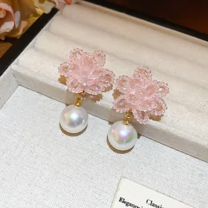 Dettaglio dei orecchini a fiore di cristallo intrecciati rosa con perle lucide.