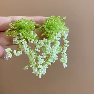 Close-up detail of handmade glass beaded tassel earrings in green and white pastoral style