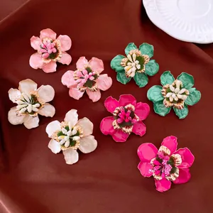 Nahaufnahme bunter Blumen-Ohrstecker aus Metall-Emaille auf einer dunklen Stoffoberfläche.
