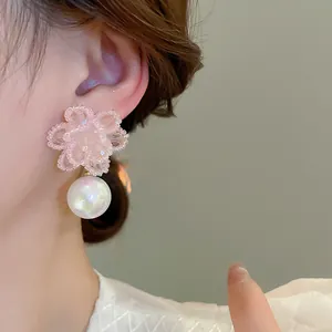 Macro di delicati orecchini intrecciati a fiore rosa con gocce di perle iridescenti