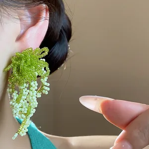 Detailed close-up view of elegant handmade green and white glass beaded tassel earrings on ear