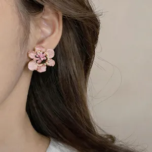 Nahaufnahme eleganter rosa Emaille-Blumenohrringe, die von einem Modell getragen werden.