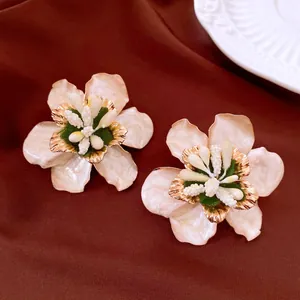Nahaufnahme eleganter Ohrstecker in Blumenform aus weißer Emaille mit Goldakzenten.