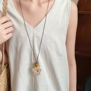 Detail of vintage ethnic style woven flower pendant necklace on a beige linen dress