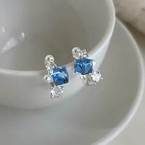 Detail shot of blue cubic zircon earrings with pearls and silver setting on white cup.