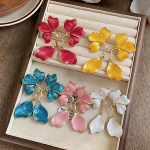 Detail view of five pairs of colorful enamel flower earrings in a beige display tray