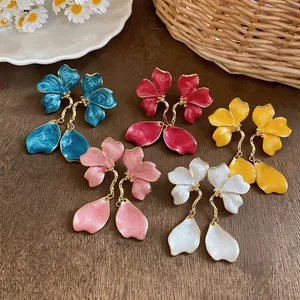 Detailed view of colorful enamel flower tassel earrings in five vibrant shades on a wooden base