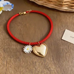 Detail view of red rope necklace with a gold heart pendant and daisy charm