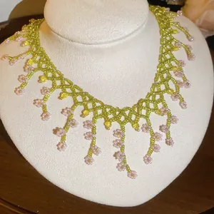 Close-up of a handmade green and pink beaded flower fringe necklace on a display stand