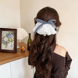 Detail of a Korean style white lace and blue gingham bow hair clip worn on long wavy hair.
