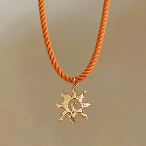 Detail of golden sun pendant with vibrant orange twisted rope chain necklace.