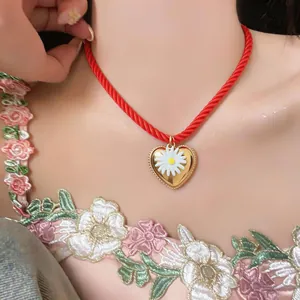 Close-up detail of a red twisted rope necklace featuring a gold heart and white daisy pendant