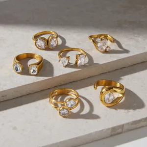 Collection of elegant gold stainless steel rings with zircon stones on a stone surface.