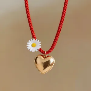 Close-up view of a vibrant red cord necklace with a gold heart pendant and white daisy charm