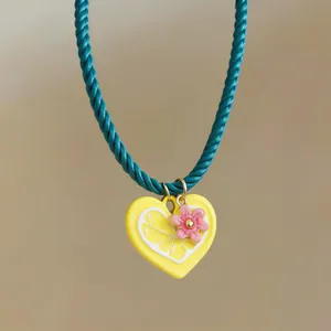 Close-up of a yellow heart lemon pendant with a pink flower charm on a teal braided cord