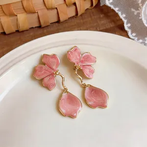 Detailed close-up view of pink enamel flower earrings with gold-toned petal drops on a plate.
