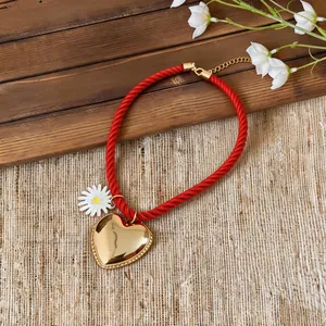 Detailed view of red braided rope necklace with gold heart and daisy pendant