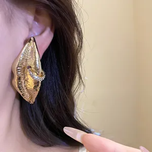 Close-up of oversized gold-plated lip stud earrings with sparkling rhinestone ring detail