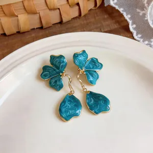 Detailed view of teal floral enamel earrings with golden tassels on a white plate