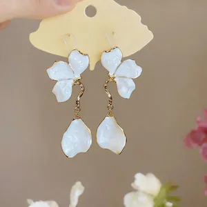 Close-up of elegant white oil-dripped flower earrings with gold-plated fringe and petals.
