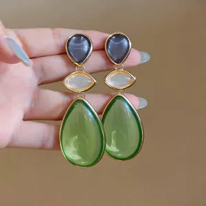 Close-up of elegant resin teardrop earrings featuring green and grey stones with gold plating