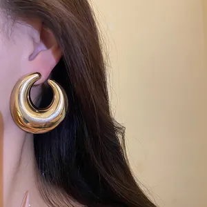 Primo piano di orecchini a cerchio dorati spessi con finitura lucida e design cavo su modella.