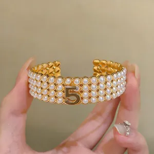 Dettaglio di bracciale rigido dorato con quattro file di perle e il numero 5 centrale