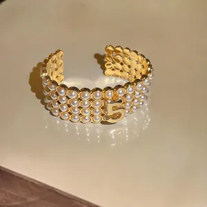 Dettaglio di bracciale rigido vintage in oro con tre file di perle e il numero 5