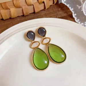Detail shot of elegant green and grey resin water drop earrings in a gold setting