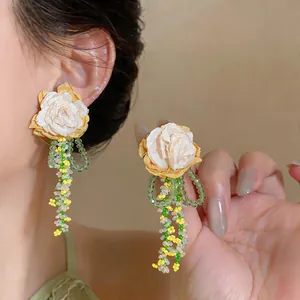 Close-up detail of cream fabric flower earrings with green glass bead tassels on model