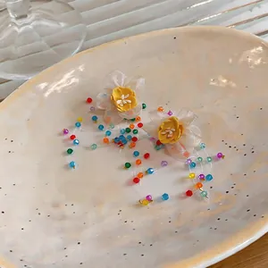 Close-up of handmade floral earrings with colorful beaded tassels on a ceramic plate.