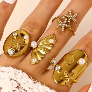 Détail de bagues en acier doré avec étoiles de mer, coquillages, zircons et perles