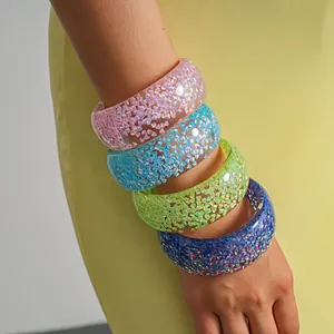 Macro detail of four colorful iridescent resin chunky bangles worn on arm.