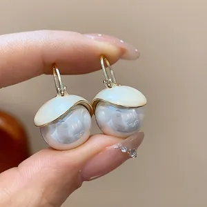 Close-up of French style pearl drop earrings with creamy enamel cap and gold hooks