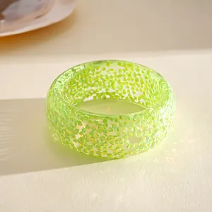 Macro detail view of a vibrant translucent green resin bangle with iridescent glitter inclusions.