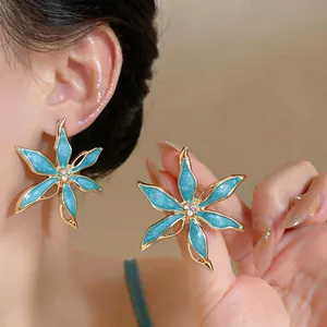 Dettaglio degli orecchini a fiore in smalto blu con strass scintillanti al centro