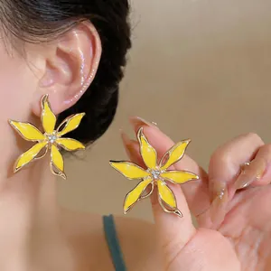 Dettaglio squisito di orecchini a fiore in smalto giallo con strass al centro.