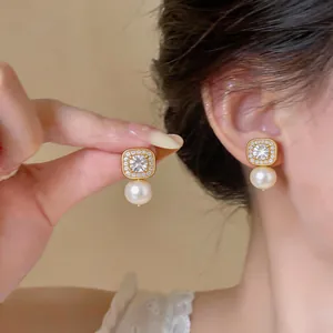 Close-up of elegant gold-toned square zircon and pearl drop earrings on a model's ear