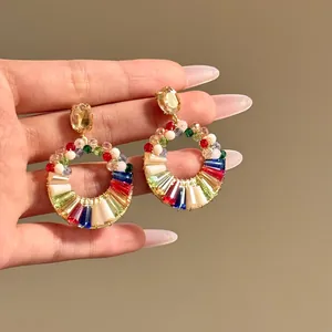 Dettaglio di orecchini a cerchio con perle di vetro colorate e design dorato.