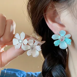 Detailed macro view of delicate blue and silver floral stud earrings shown on the ear