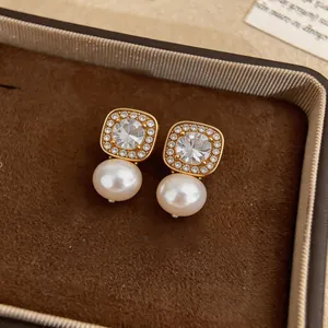 Close-up view of elegant gold-tone square zircon and pearl drop earrings in a box.