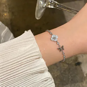 Detail view of a delicate silver bracelet with shell flower and butterfly on a wrist.