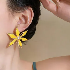 Dettaglio di un orecchino a forma di fiore in smalto giallo con strass sull'orecchio