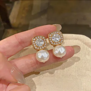 Close-up of elegant gold pearl earrings with sparkling square zircon halo details.