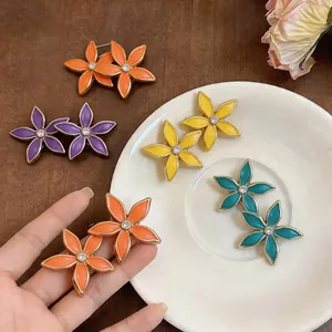 Primo piano di orecchini a fiore in smalto colorato con strass brillanti su un piatto bianco.