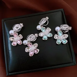 Detailed view of floral clip-on earrings with rhinestones and pearls on black leather.