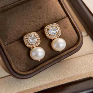 Macro view of gold-plated zircon earrings with dangling round pearls in jewelry box