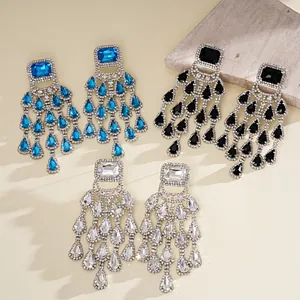 Close-up of square crystal earrings with elegant teardrop tassels in blue, black, and white.
