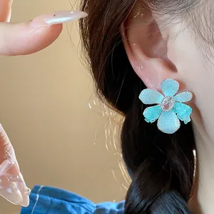 Detailed macro view of blue glass flower earring with zircon center worn on a model's ear