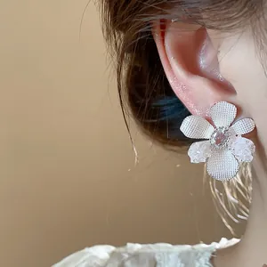 Close-up detail of elegant silver flower stud earring with central zircon stone on ear